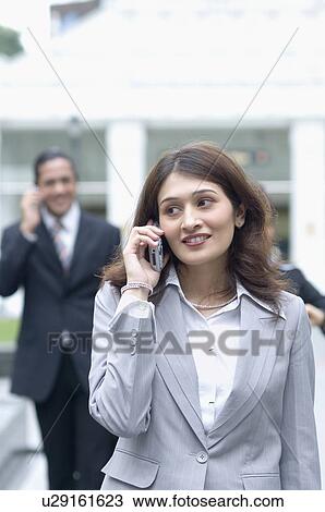 Businesswoman talking on a mobile phone with a businessman in the background View Large Photo Image Stock Image - Businesswoman talking on a mobile phone with a businessman in the background. Fotosearch