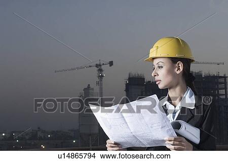 Picture - Businesswoman wearing a hardhat and holding a blueprint. Fotosearch