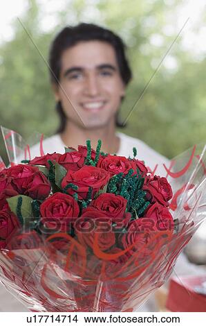 Picture - Close-up of a bouquet of flowers with a young man smiling in the background. Fotosearch