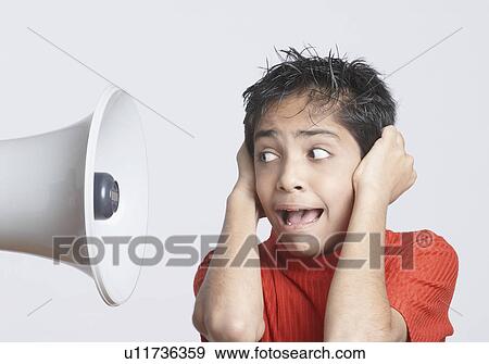 Stock Photo - Close-up of a boy covering his ears with his hands and looking at a megaphone. Fotosearch