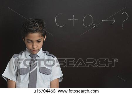 Stock Image - Close-up of a boy in front of a blackboard and looking down. Fotosearch