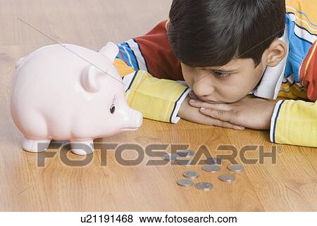 Stock Photo - Close-up of a boy lying in front of a piggy bank. Fotosearch