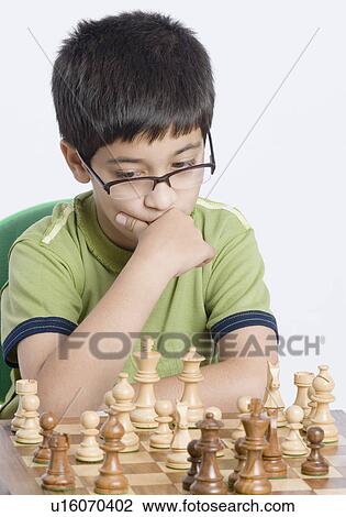 Stock Image - Close-up of a boy playing chess with his hand on his chin. Fotosearch