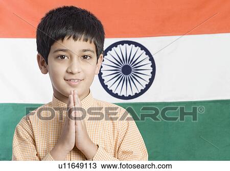 Stock Image - Close-up of a boy standing in front of the Indian flag with his hands folded. Fotosearch