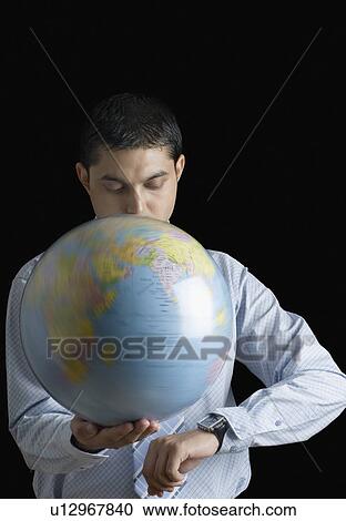 Stock Image - Close-up of a businessman holding a spinning globe and checking the time. Fotosearch