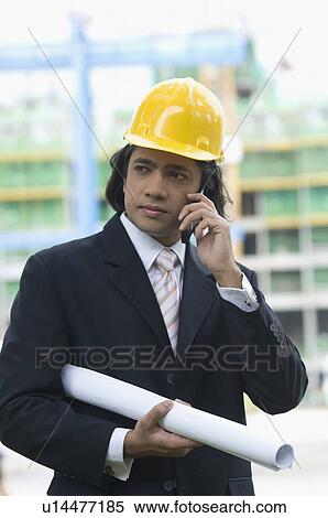 Stock Photography - Close-up of a businessman holding a blueprint and talking on a mobile phone. Fotosearch