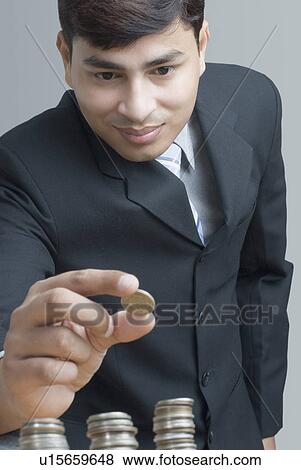 Stock Photo - Close-up of a businessman holding an Indian coin over the stacks of coin. Fotosearch