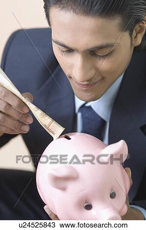 Close-up of a businessman putting money in a piggy bank View Large Photo Image Stock Image - Close-up of a businessman putting money in a piggy bank. Fotosearch