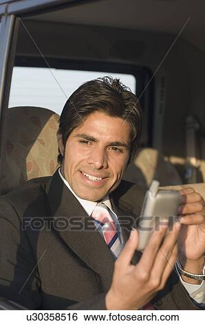 Stock Photograph - Close-up of a businessman using a personal data assistant in a car. Fotosearch
