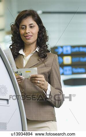 Picture - Close-up of a businesswoman standing in front of an automatic ticket machine and holding her boarding pass. Fotosearch