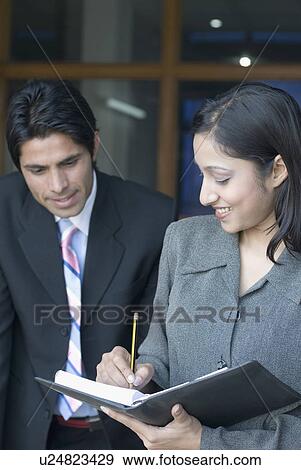 Close-up of a businesswoman writing in a diary with a businessman standing beside her View Large Photo Image Stock Photo - Close-up of a businesswoman writing in a diary with a businessman standing beside her. Fotosearch