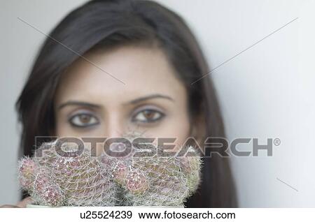 Stock Photo - Close-up of a cactus plant in front of a young woman's face. Fotosearch