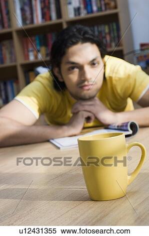 Close-up of a cup with a young man lying on the floor of a library in the background View Large Photo Image Stock Photography - Close-up of a cup with a young man lying on the floor of a library in the background. Fotosearch