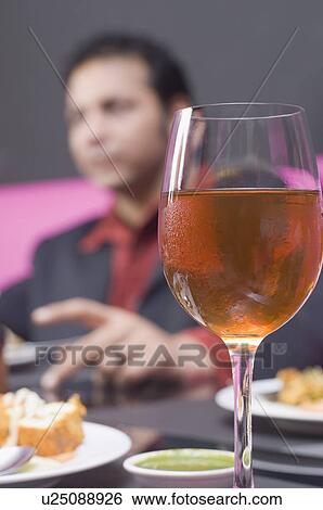 Stock Photograph - Close-up of a glass of wine with a young man sitting in the background. Fotosearch