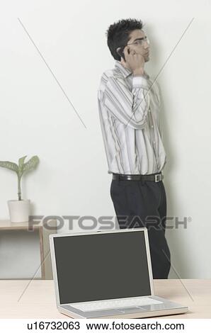 Stock Image - Close-up of a laptop with a businessman talking on a mobile phone in the background. Fotosearch