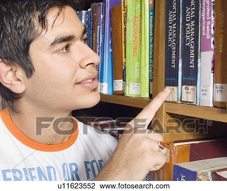 Stock Image - Close-up of a male college student selecting a book from a library shelf. Fotosearch