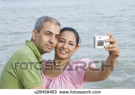 Close-up of a mid adult couple taking a photograph of themselves View Large Photo Image Stock Image - Close-up of a mid adult couple taking a photograph of themselves. Fotosearch