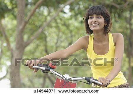 Stock Image - Close-up of a mid adult woman holding a bicycle and smiling. Fotosearch