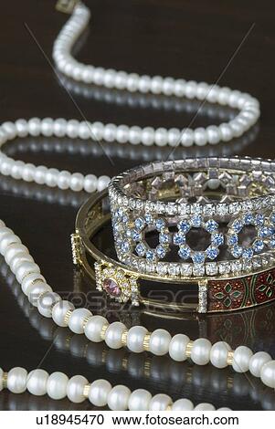 Stock Image - Close-up of a pearl necklace with two gold bracelets. Fotosearch
