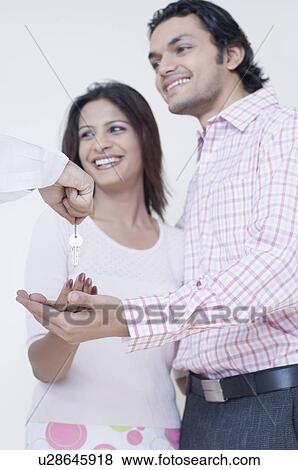 Stock Photo - Close-up of a person's hand extending keys to a young couple. Fotosearch