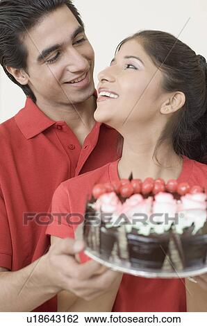Close-up of a young couple holding a chocolate cake and looking at each other View Large Photo Image Stock Image - Close-up of a young couple holding a chocolate cake and looking at each other. Fotosearch