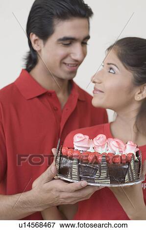 Close-up of a young couple holding a chocolate cake and looking at each other View Large Photo Image Stock Photo - Close-up of a young couple holding a chocolate cake and looking at each other. Fotosearch