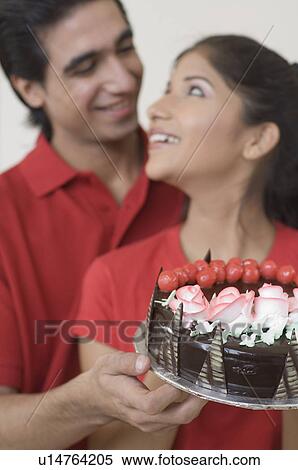 Stock Photography - Close-up of a young couple holding a chocolate cake and looking at each other. Fotosearch