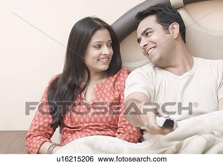 Close-up of a young couple sitting on a bed and smiling View Large Photo Image Stock Photograph - Close-up of a young couple sitting on a bed and smiling. Fotosearch