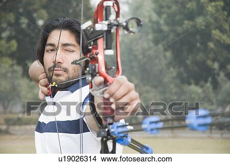 Picture - Close-up of a young man aiming with a bow and arrow. Fotosearch
