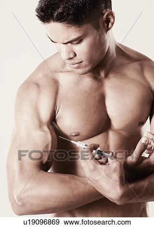 Close-up of a young man holding a syringe against his biceps View Large Photo Image Stock Photo - Close-up of a young man holding a syringe against his biceps. Fotosearch
