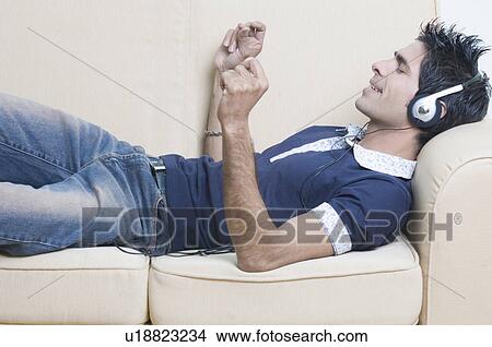 Close-up of a young man lying on a couch and listening to music View Large Photo Image Picture - Close-up of a young man lying on a couch and listening to music. Fotosearch
