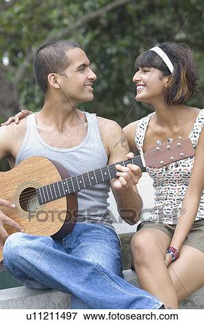 Close-up of a young man playing a guitar with a mid adult woman sitting beside him View Large Photo Image Stock Photo - Close-up of a young man playing a guitar with a mid adult woman sitting beside him. Fotosearch