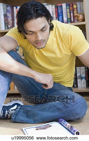 Close-up of a young man sitting on the floor and reading a magazine View Large Photo Image Stock Photograph - Close-up of a young man sitting on the floor and reading a magazine. Fotosearch