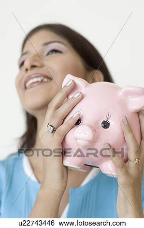 Close-up of a young woman holding a piggy bank and smiling View Large Photo Image Stock Photograph - Close-up of a young woman holding a piggy bank and smiling. Fotosearch