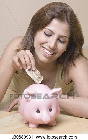 Close-up of a young woman inserting money into a piggy bank View Large Photo Image Stock Image - Close-up of a young woman inserting money into a piggy bank. Fotosearch
