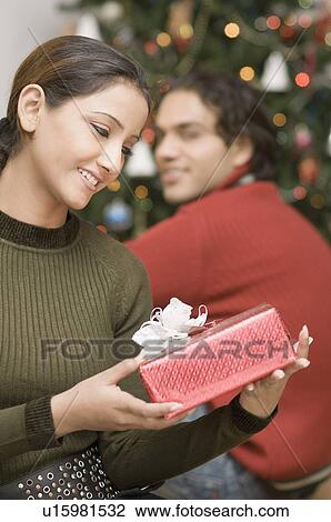 Close-up of a young woman looking at a Christmas present with a young man sitting beside her View Large Photo Image Stock Image - Close-up of a young woman looking at a Christmas present with a young man sitting beside her. Fotosearch