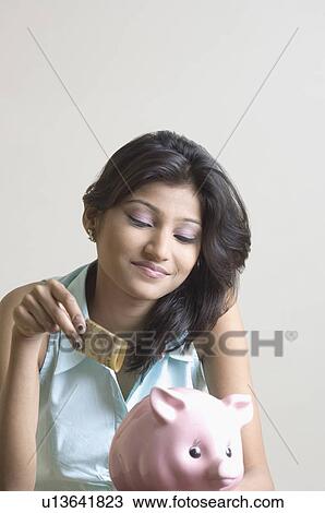 Stock Image - Close-up of a young woman putting money in a piggy bank. Fotosearch