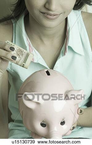 Stock Photo - Close-up of a young woman putting money in a piggy bank. Fotosearch