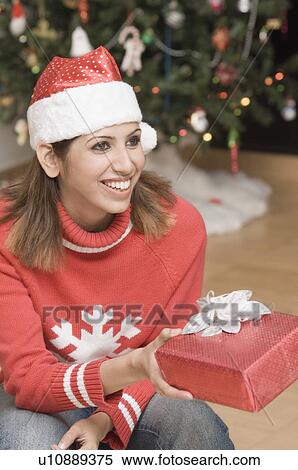 Stock Photography - Close-up of a young woman smiling and giving a Christmas present. Fotosearch