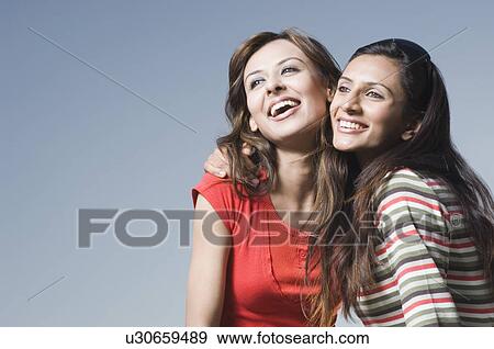 Stock Photo - Close-up of a young woman smiling with her arms around another woman. Fotosearch