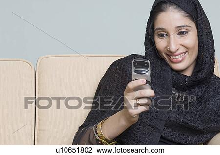 Stock Image - Close-up of a young woman using a mobile phone and smiling. Fotosearch