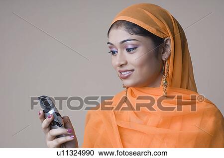 Stock Image - Close-up of a young woman using a mobile phone and smiling. Fotosearch