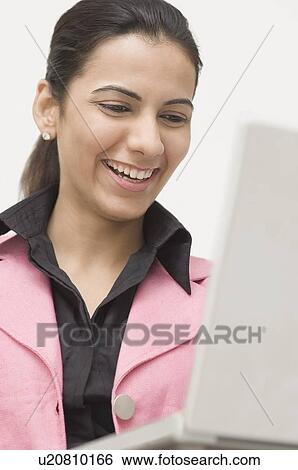 Close-up of a young woman using a laptop and smiling View Large Photo Image Stock Photograph - Close-up of a young woman using a laptop and smiling. Fotosearch