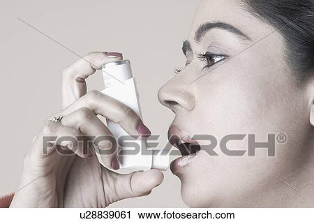 Stock Image - Close-up of a young woman using an inhaler. Fotosearch