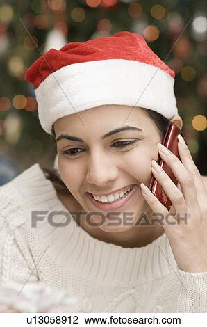 Stock Image - Close-up of a young woman wearing a Santa hat and talking on a mobile phone. Fotosearch