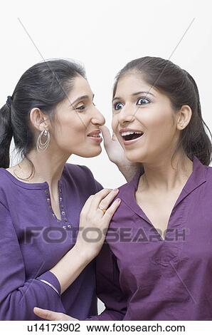 Stock Image - Close-up of a young woman whispering into another young woman's ear. Fotosearch