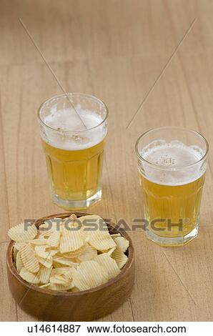 Stock Photo - Close-up of two beer glasses with a bowl of potato chips. Fotosearch