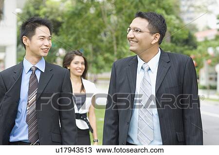 Close-up of two businessmen smiling with a businesswoman standing behind them View Large Photo Image Stock Image - Close-up of two businessmen smiling with a businesswoman standing behind them. Fotosearch