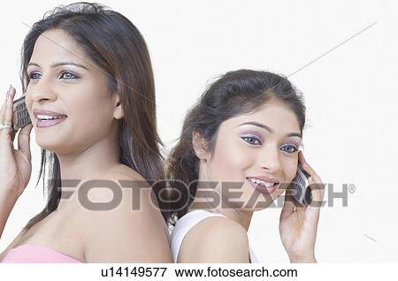 Stock Photo - Close-up of two young women back to back and talking on mobile phones. Fotosearch