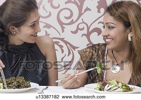 Stock Image - Close-up of two young women eating food with chopsticks. Fotosearch